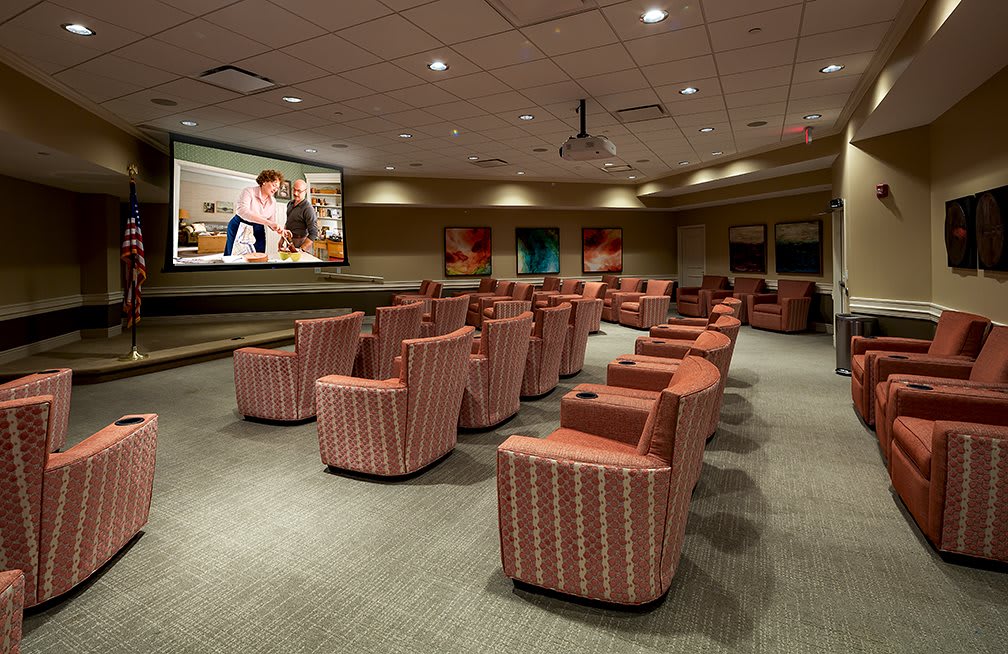 A cozy indoor movie theater with comfortable seating arranged in front of a large projector screen.