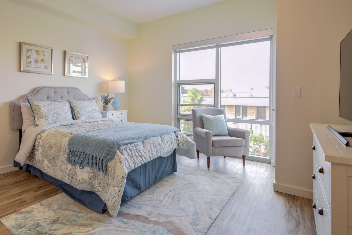 A well-lit bedroom featuring a neatly made bed, accent chair by the window, and elegant decor.