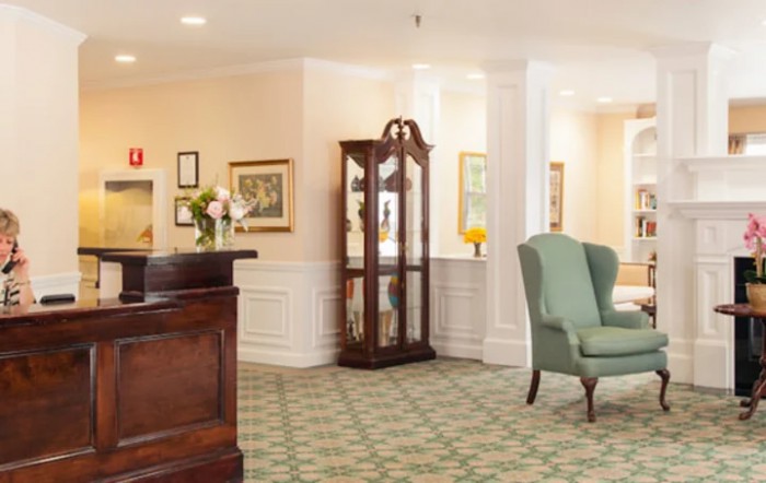 A traditional reception area with a wooden desk, green armchair, and decorative cabinet.