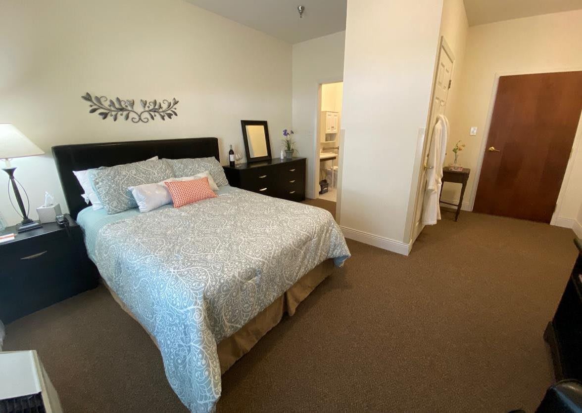 A cozy bedroom with a neatly made bed and decorative pillows, featuring a dresser with a mirror.
