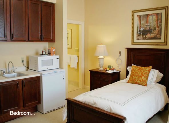 A cozy hotel room featuring a bed, wooden furniture, microwave, and refrigerator.