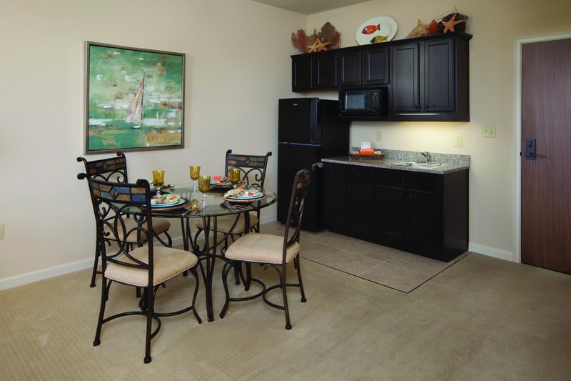 A compact kitchen with dark cabinets and a glass dining table set for a meal.