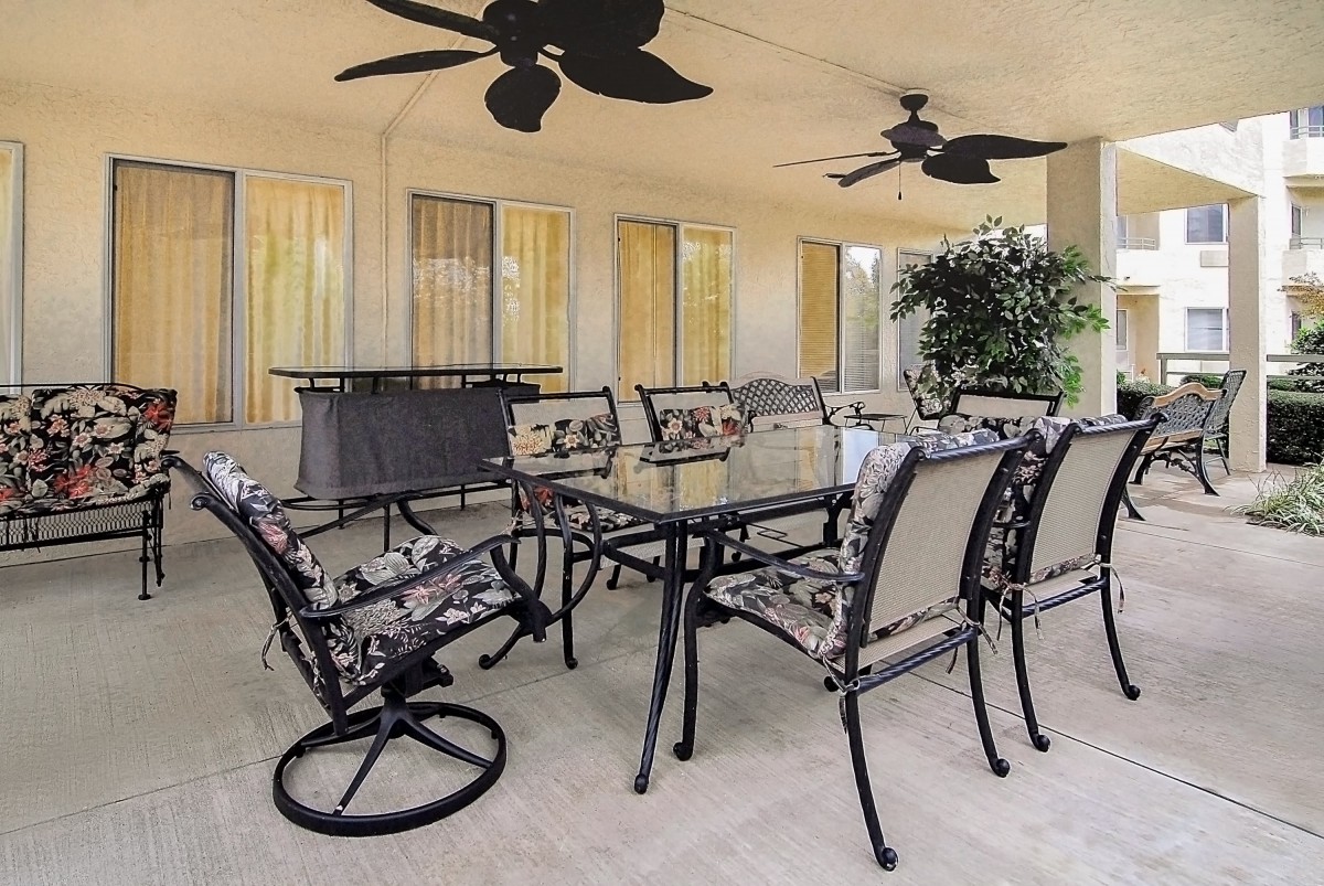 A stylish outdoor patio dining area with a glass table and chairs under ceiling fans.