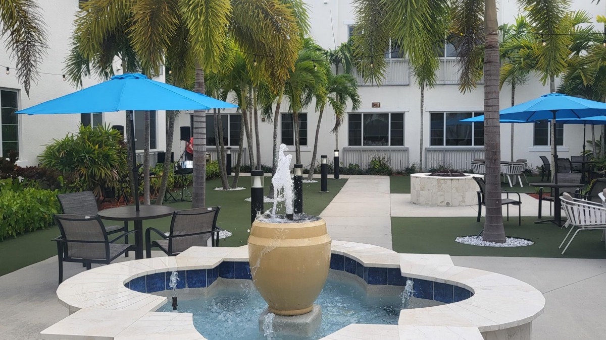 A tranquil courtyard featuring a central fountain surrounded by palm trees and outdoor seating.