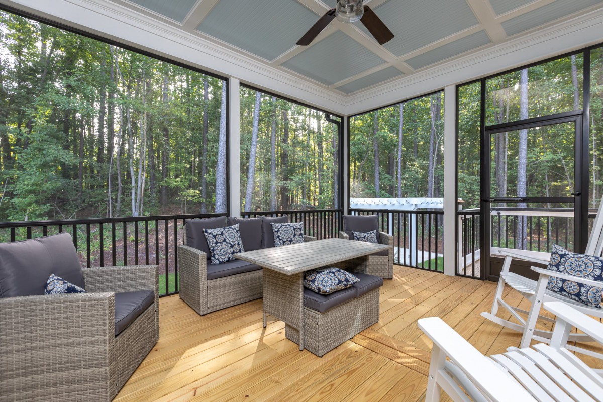 A cozy screened porch with wicker furniture overlooks a lush forest backdrop.