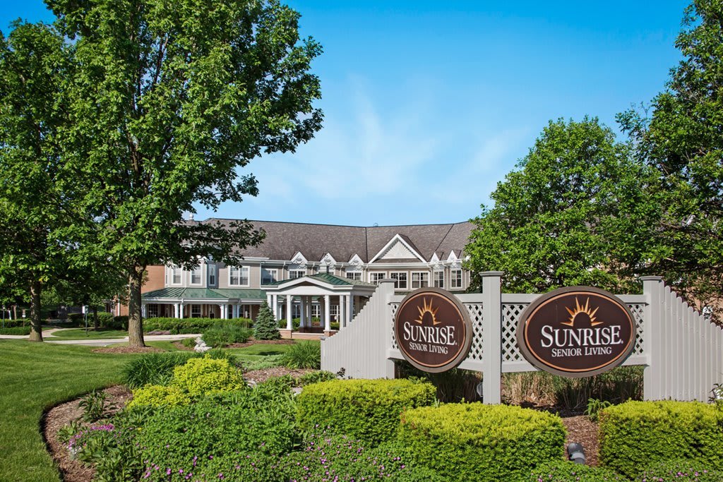 A well-landscaped building with prominent signage in front, surrounded by trees and greenery under a clear blue sky.