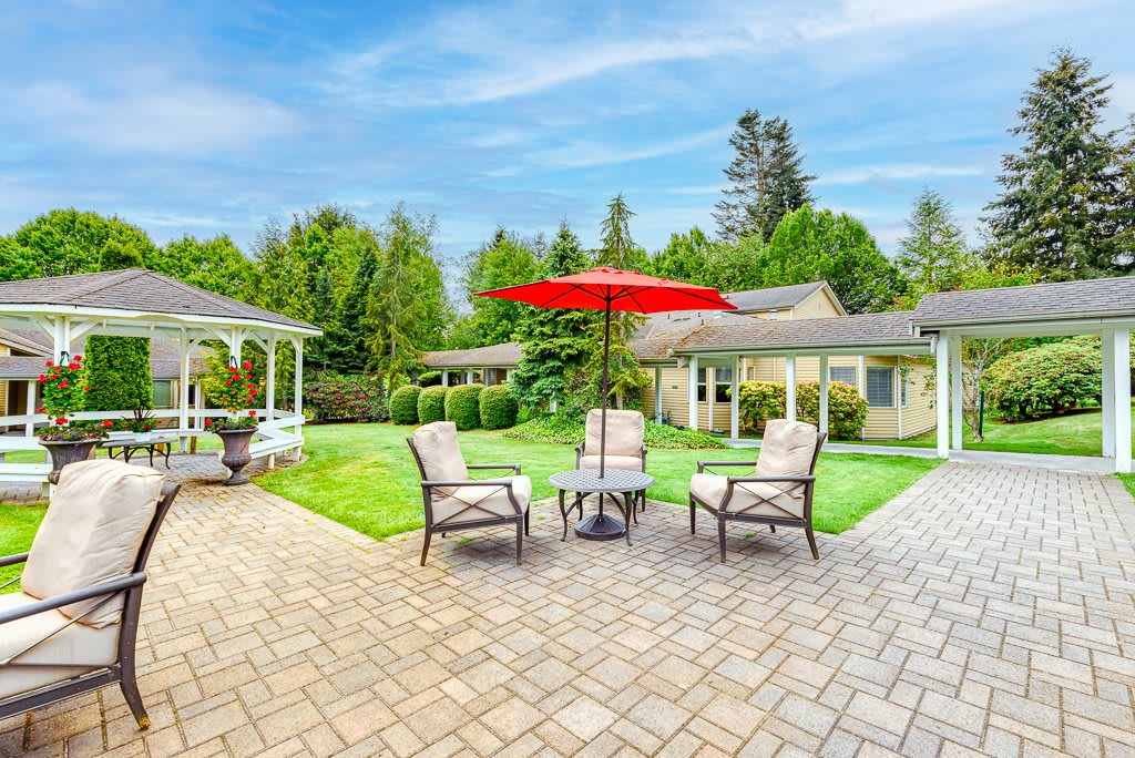 A spacious patio with comfortable outdoor seating and a red umbrella, surrounded by a lush garden and gazebo.