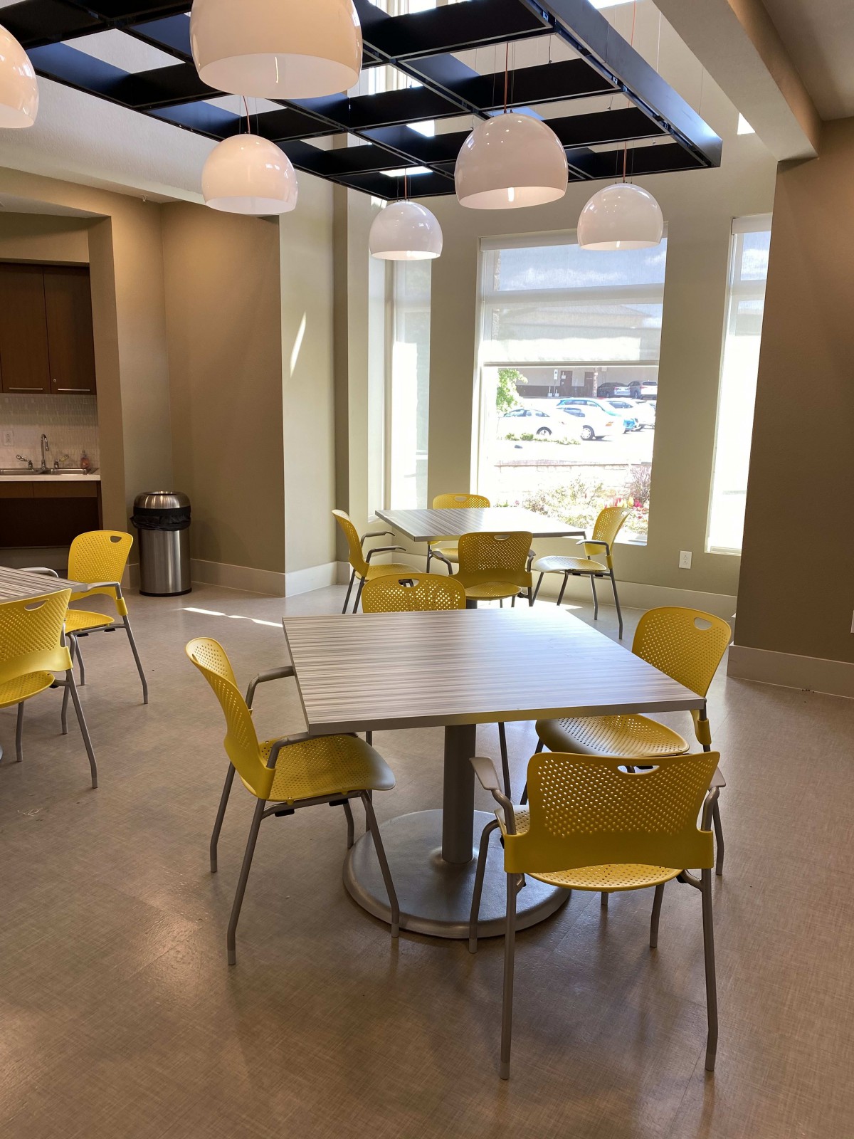 A modern cafeteria with yellow chairs and white tables.