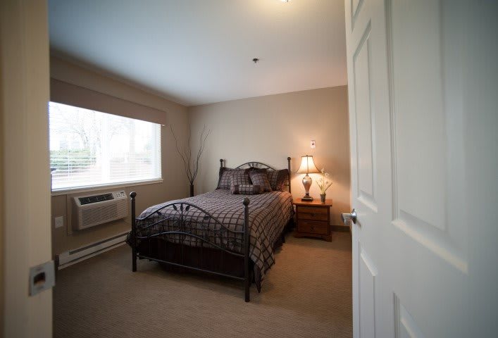 A cozy bedroom featuring a bed with a metal frame, a nightstand with a lamp, and a large window letting in natural light.