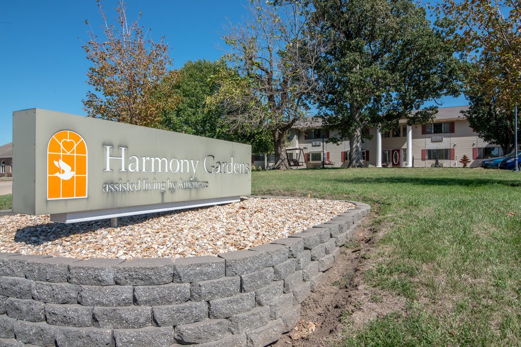 A landscaped area in front of a building, featuring a sign with trees and a clear blue sky.
