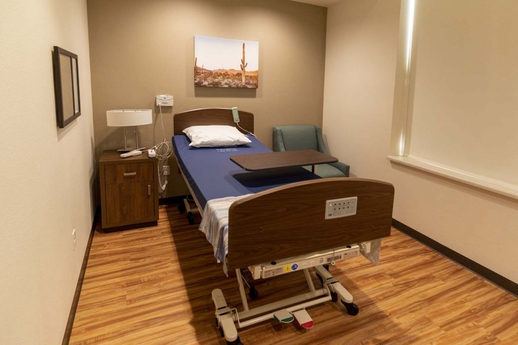 An empty hospital room with a single bed and wooden floor.