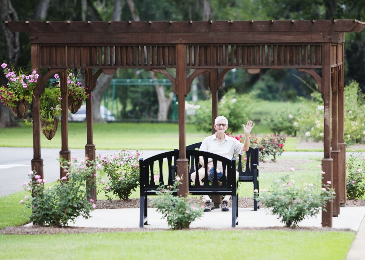 A person sitting on a bench under a gazebo in a peaceful park setting.