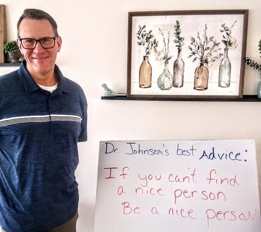 A man stands next to a sign with inspirational advice in a home setting.