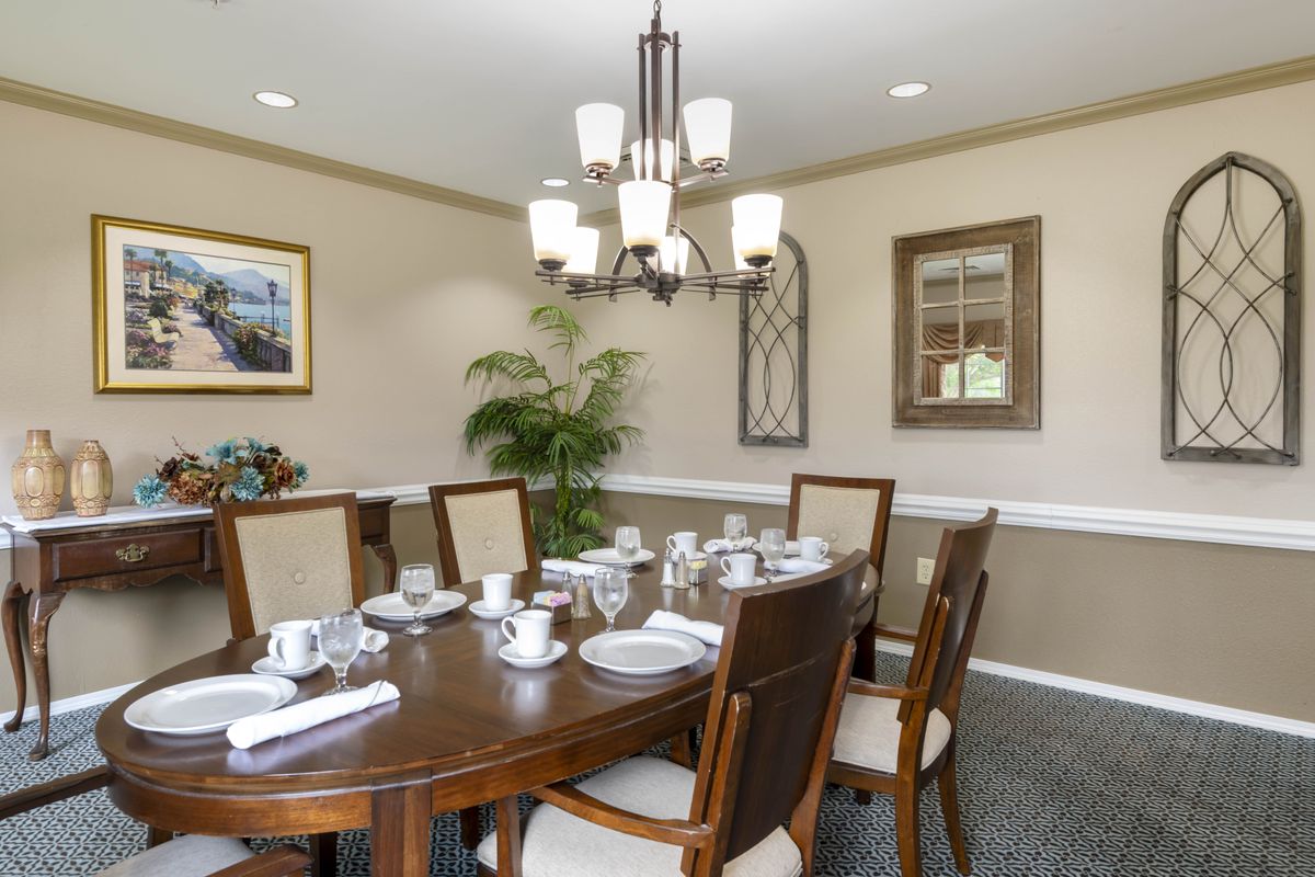 A neatly set dining room with a wooden table, upholstered chairs, and a central chandelier.