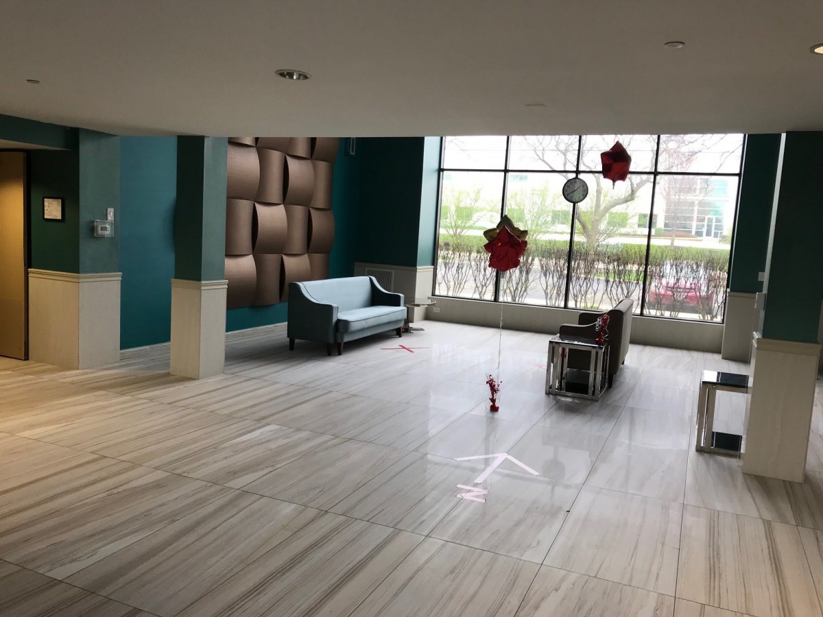 A spacious and modern lobby area with a sofa, table, and decorative elements, illuminated by natural light from large windows.