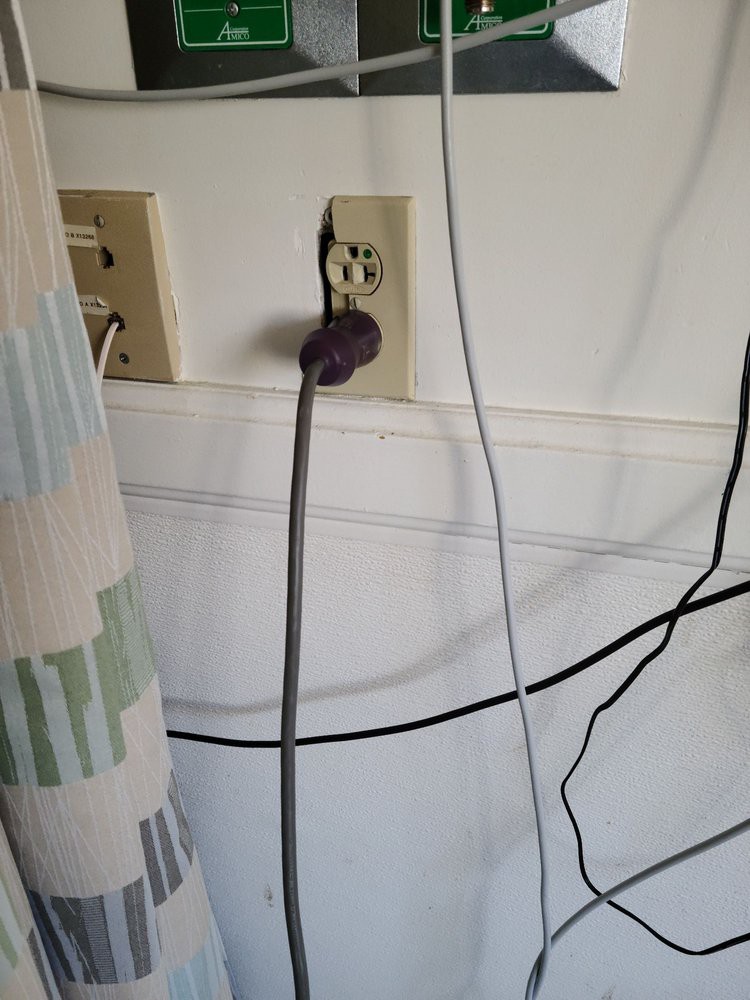 A collection of power cords plugged into a wall outlet with visible wires and a nearby curtain.