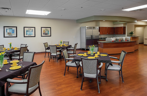 A spacious dining area featuring neatly arranged tables and chairs, with a modern kitchen in the background.