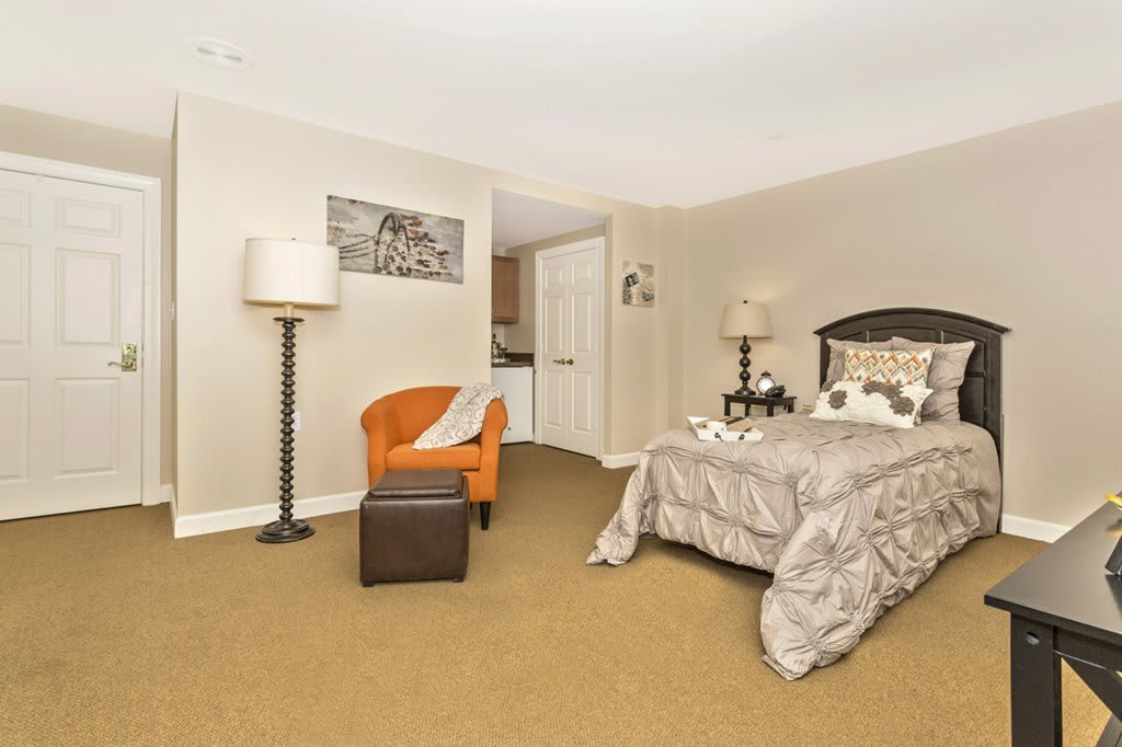 A cozy bedroom featuring a comfortable bed, an orange chair with a footrest, and elegant decor.