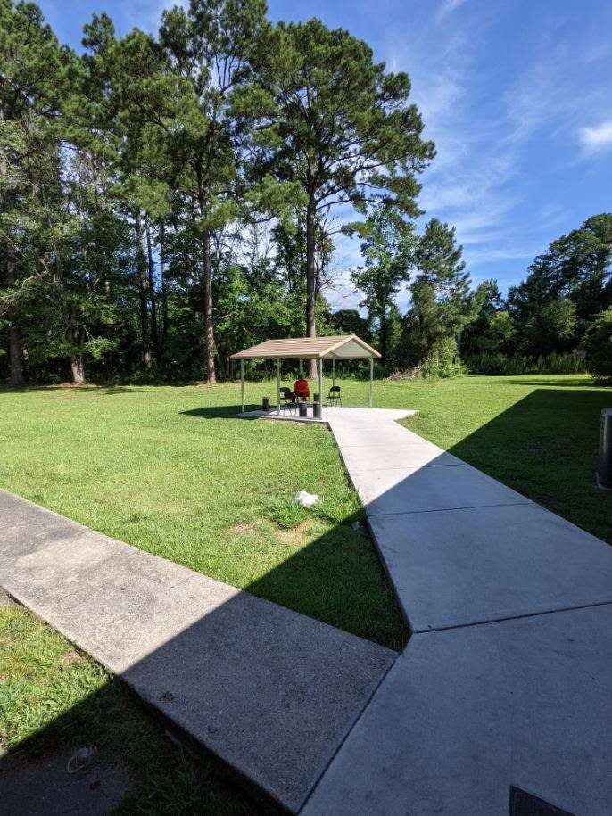 A peaceful park scene with a pavilion, surrounded by trees and grass under a clear blue sky.