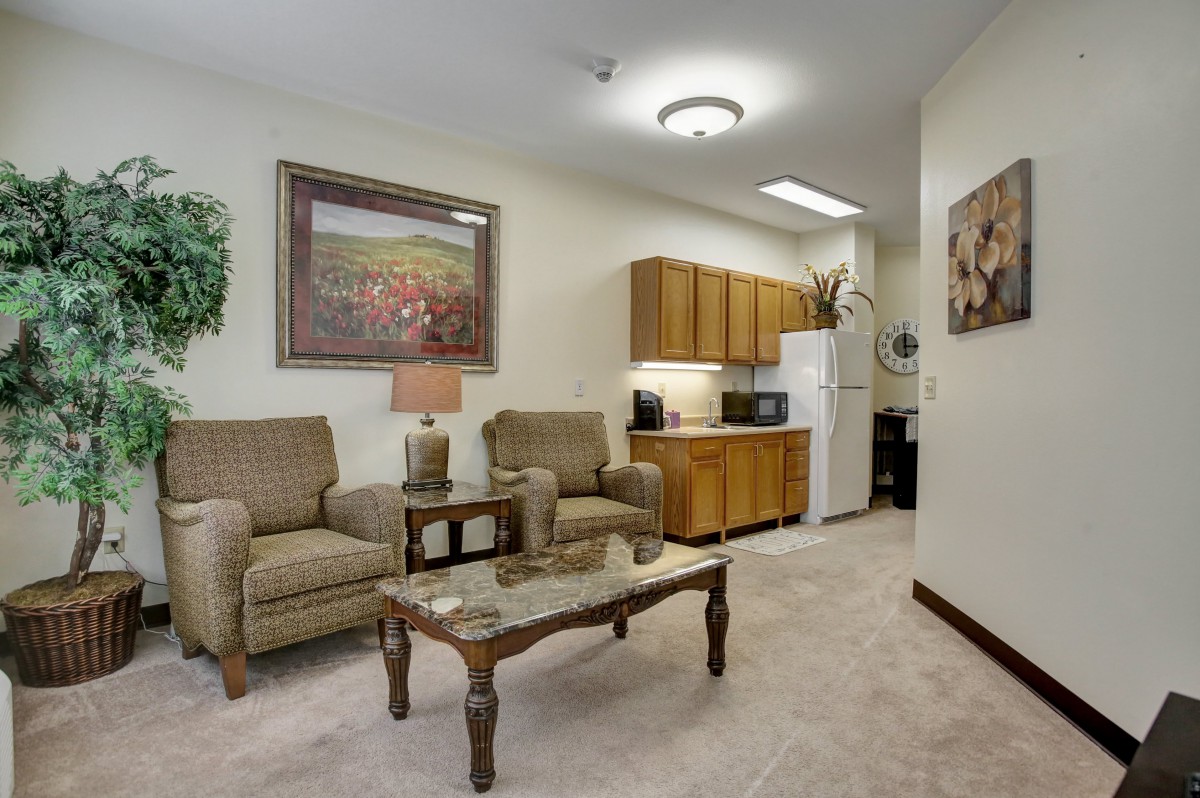 A cozy living area with comfortable seating, a coffee table, artwork on the walls, and a small kitchenette.