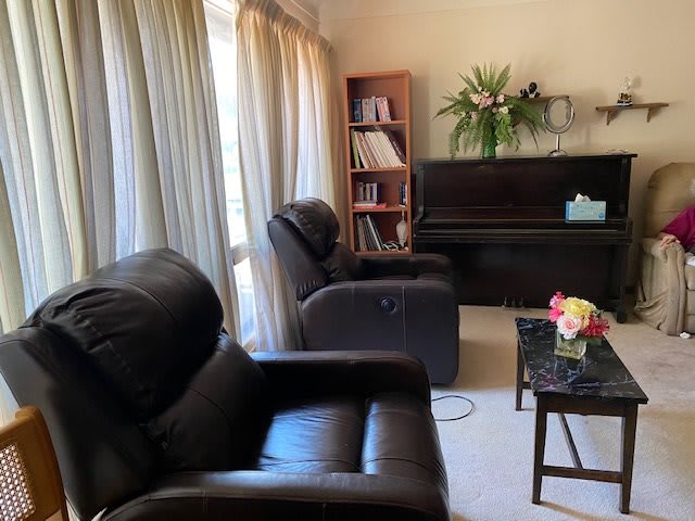 A cozy living room with a piano, armchairs, a bookshelf, and a coffee table adorned with flowers.