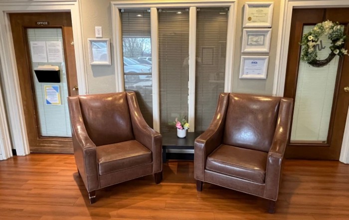 A cozy waiting area with two leather chairs and framed certificates on the wall.