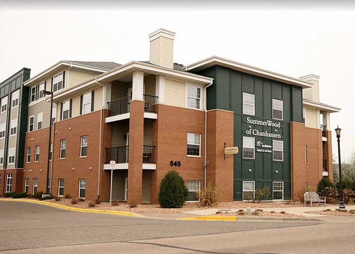 A three-story residential building with brick and green siding in an urban area.