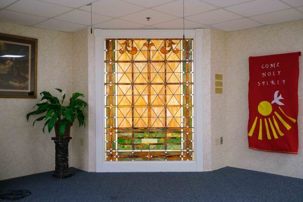 A decorative stained glass window in an interior setting with a potted plant and carpeted floor.