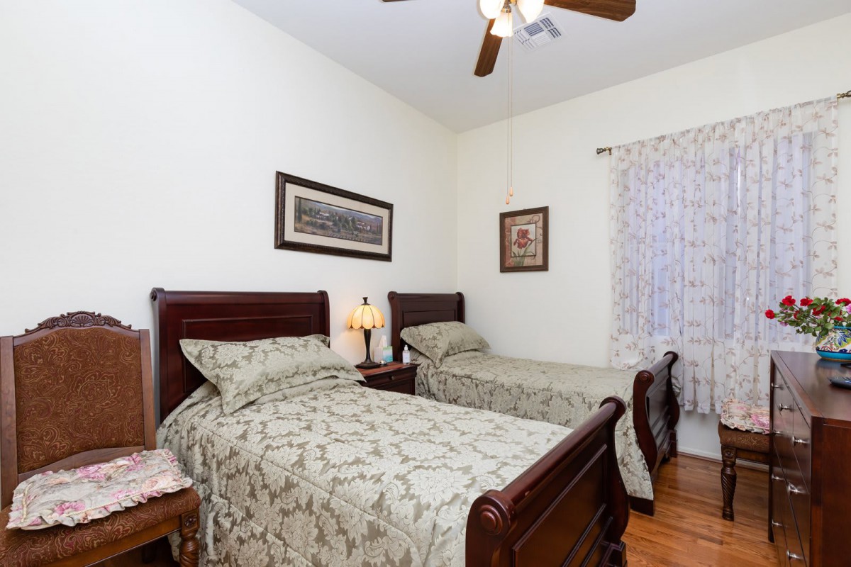 A cozy bedroom with twin beds, decorated with light green patterned bedspreads, wooden furniture, and wall art.