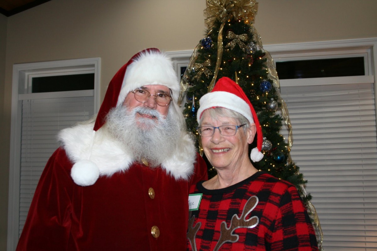 An elderly couple poses with Santa Claus in front of a decorated Christmas tree, dressed festively for the holiday season.