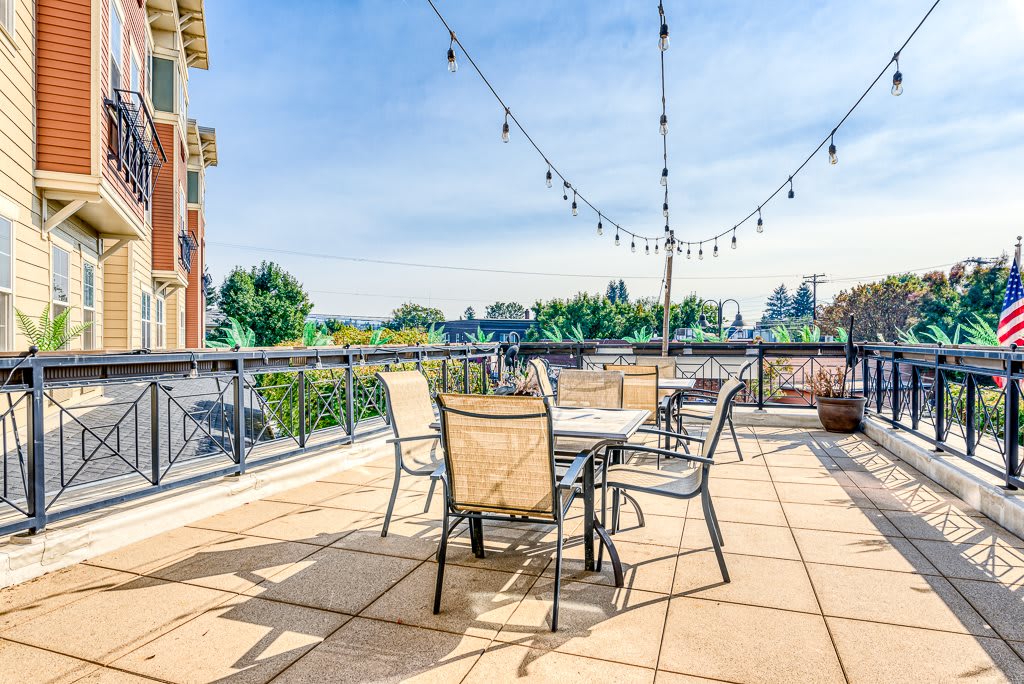 A sunny outdoor patio with tables, chairs, and string lights overlooking an urban landscape.