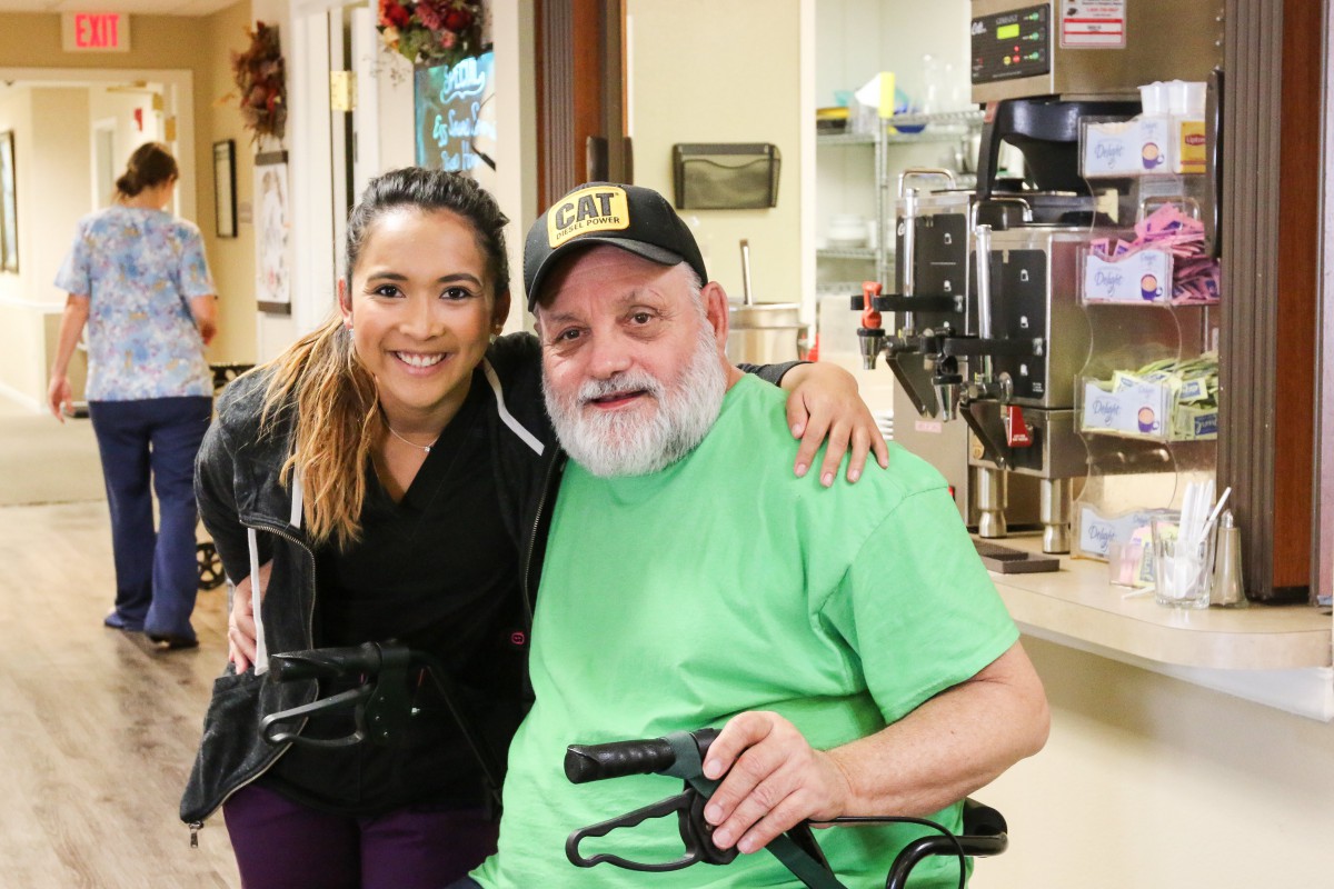 Two people smiling indoors, one seated in a wheelchair.