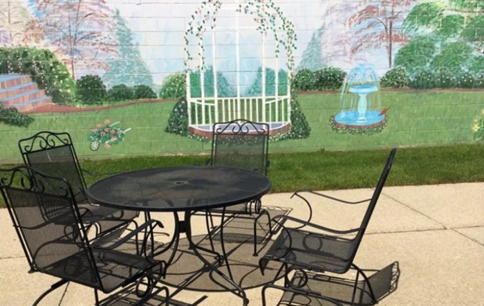 A patio set in front of a garden mural, depicting a gazebo and fountain.
