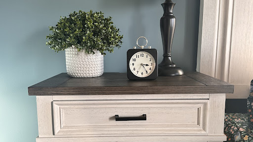 A stylish arrangement featuring a clock, a decorative plant, and a lamp on a wooden table.