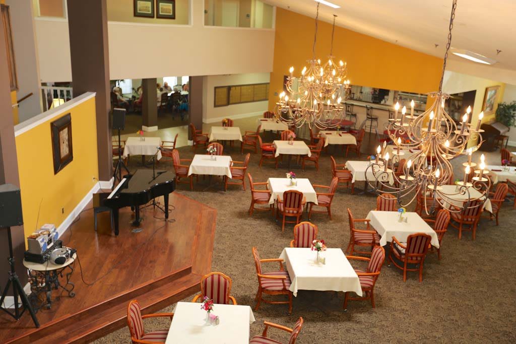 A spacious dining area featuring elegantly set tables, a grand chandelier, and a black piano.