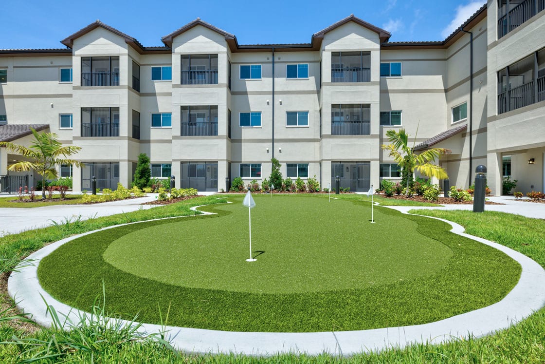 A modern apartment complex with a well-maintained putting green in the foreground.