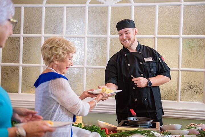 A chef is happily serving food to an elderly woman indoors.