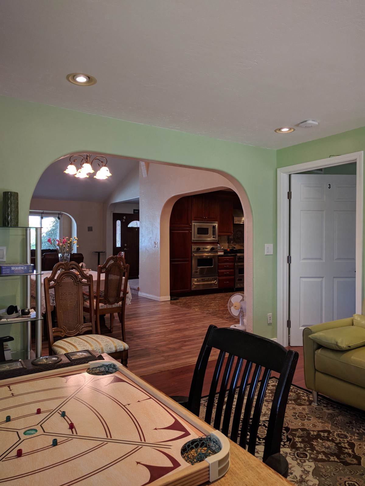 A cozy interior view featuring a living area with green walls, wooden flooring, and an archway leading to a dining room.