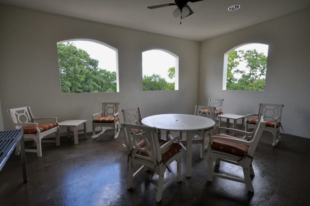 A cozy indoor dining area with a round table and chairs, illuminated by natural light through large windows.