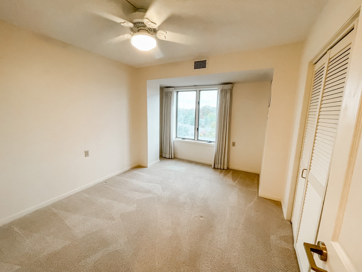 An empty room with carpet flooring, a ceiling fan, and a window with curtains.