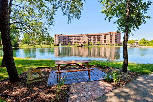 A serene view of a lake with a picnic table in the foreground and a building reflecting on the water.