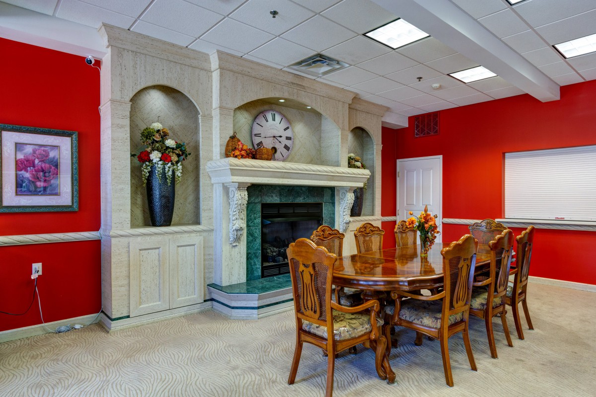 A dining room with a wooden table and chairs, featuring a decorative fireplace and red accent wall.