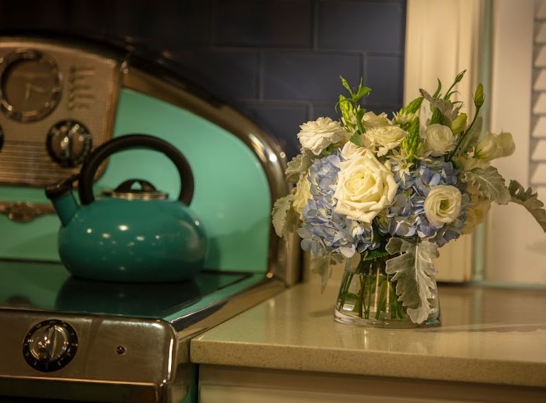 A vintage kitchen setting with a teal teapot and a bouquet of blue and white flowers.