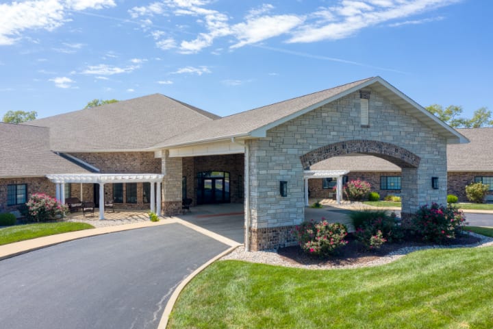 A modern building with a paved entrance and landscaped surroundings under a clear blue sky.