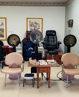 A cozy salon interior featuring hairdryers and comfortable chairs arranged around a small table with magazines.