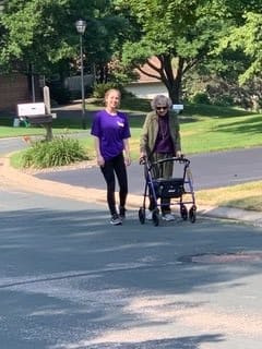 A caregiver assisting an elderly person using a walker on a sunny street.