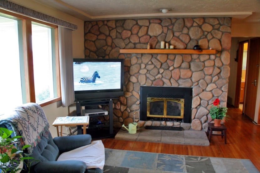 A cozy living room featuring a stone fireplace, a television, and a comfortable chair.