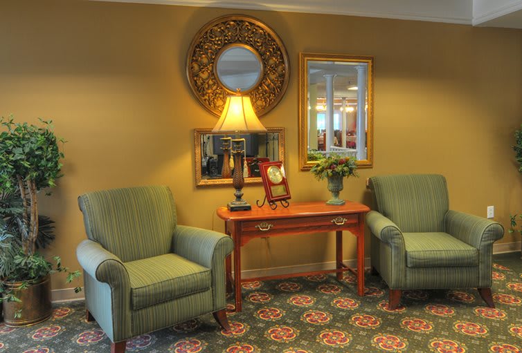 A cozy living room setup featuring two armchairs, a central table with a lamp, and decorative mirrors on the wall.