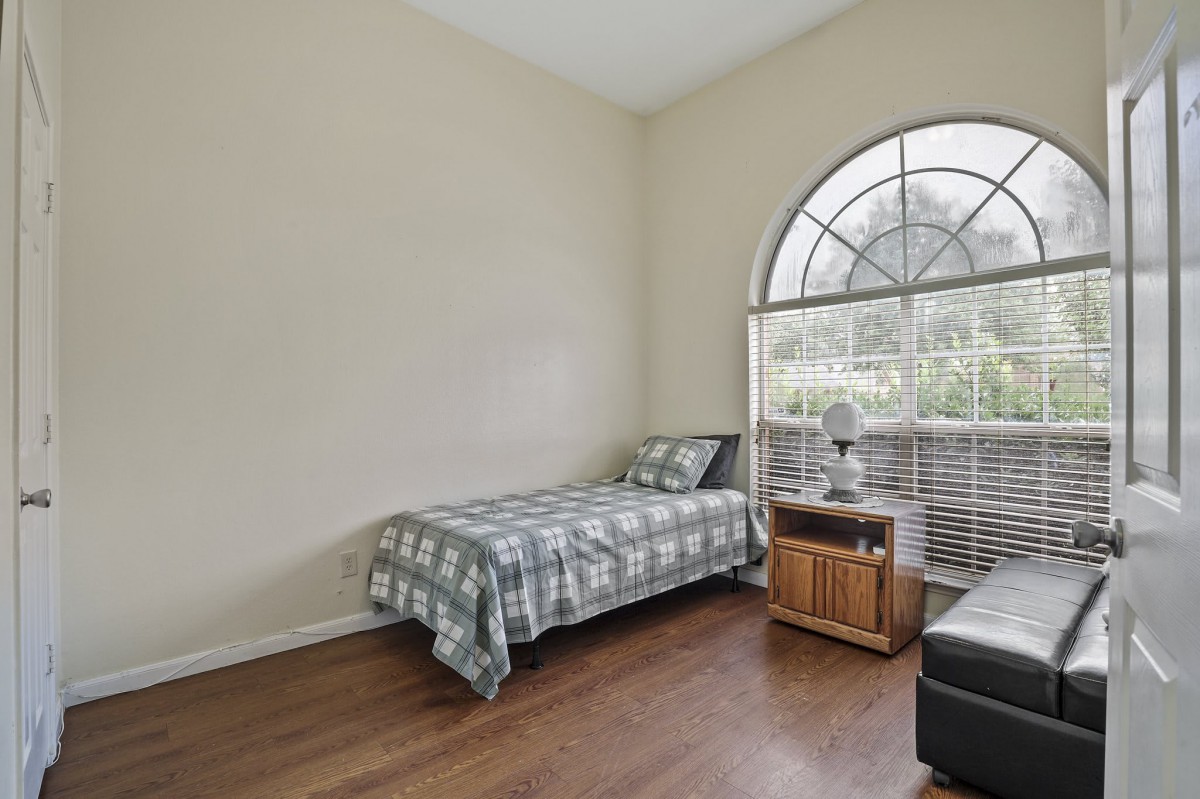 A cozy bedroom with a single bed, nightstand, and large window allowing natural light to fill the space.