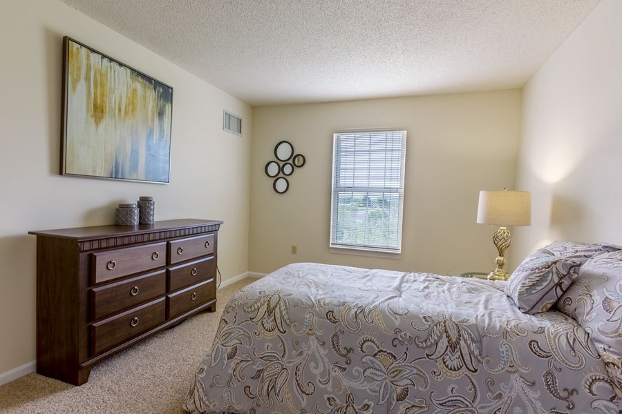 A cozy bedroom featuring a bed, dresser, window, and decorative artwork on the wall.